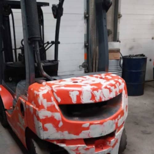 Heavy-duty orange forklift truck in a warehouse workshop.