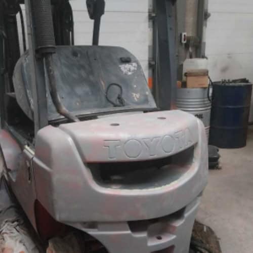 Damaged forklift truck in a warehouse or workshop setting.